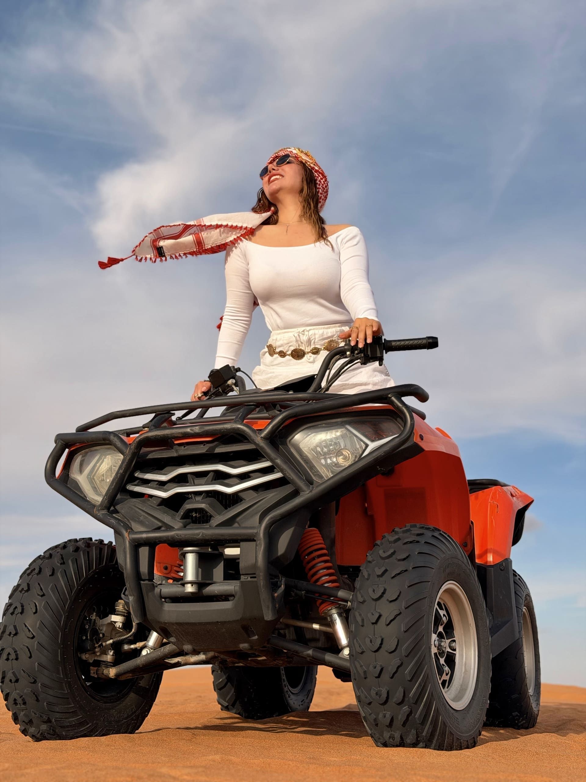 Woman on a red quad bike on the dunes, bright blue sky