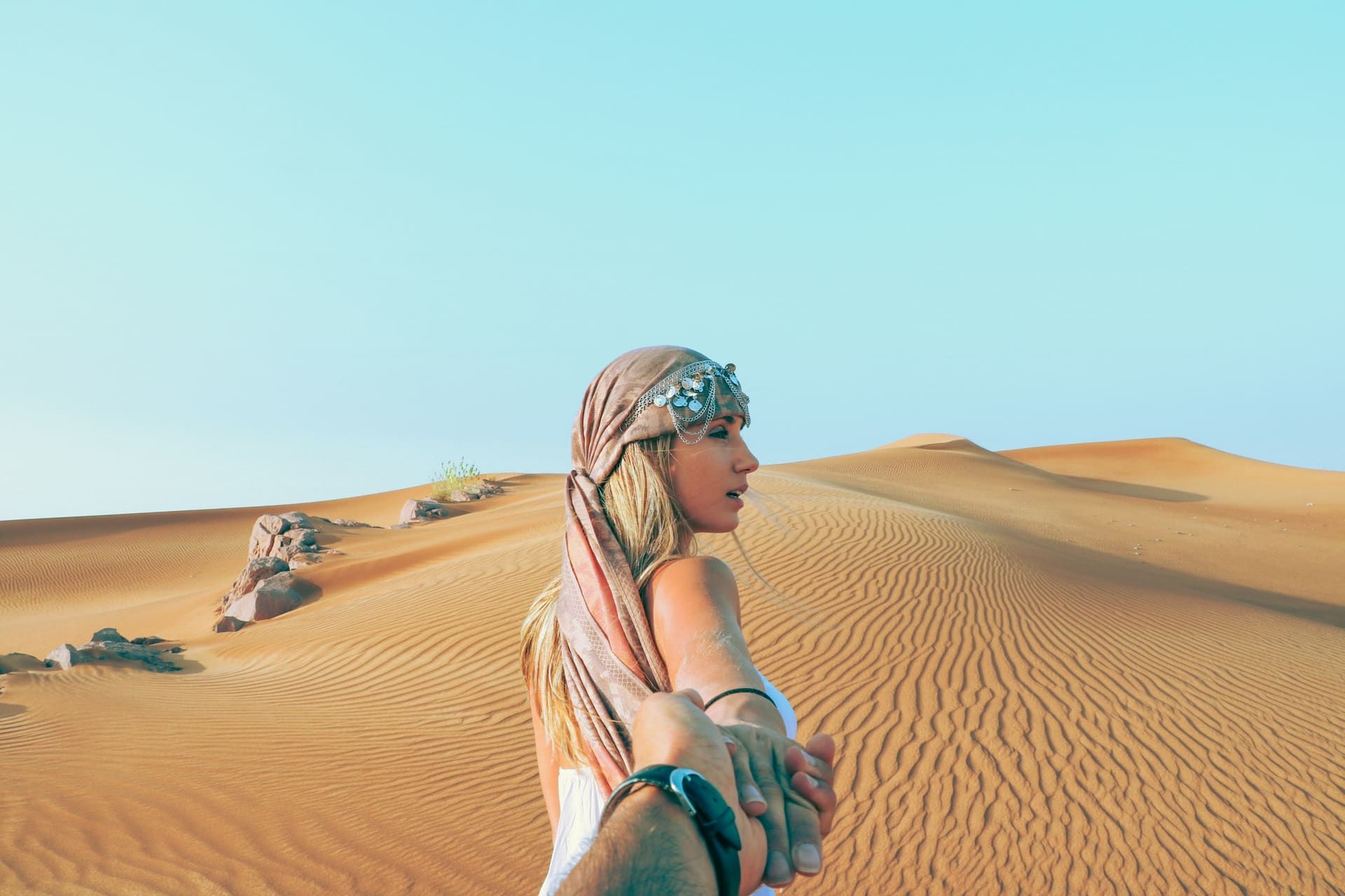 Couple holding hands walking into the dunes of the Dubai desert