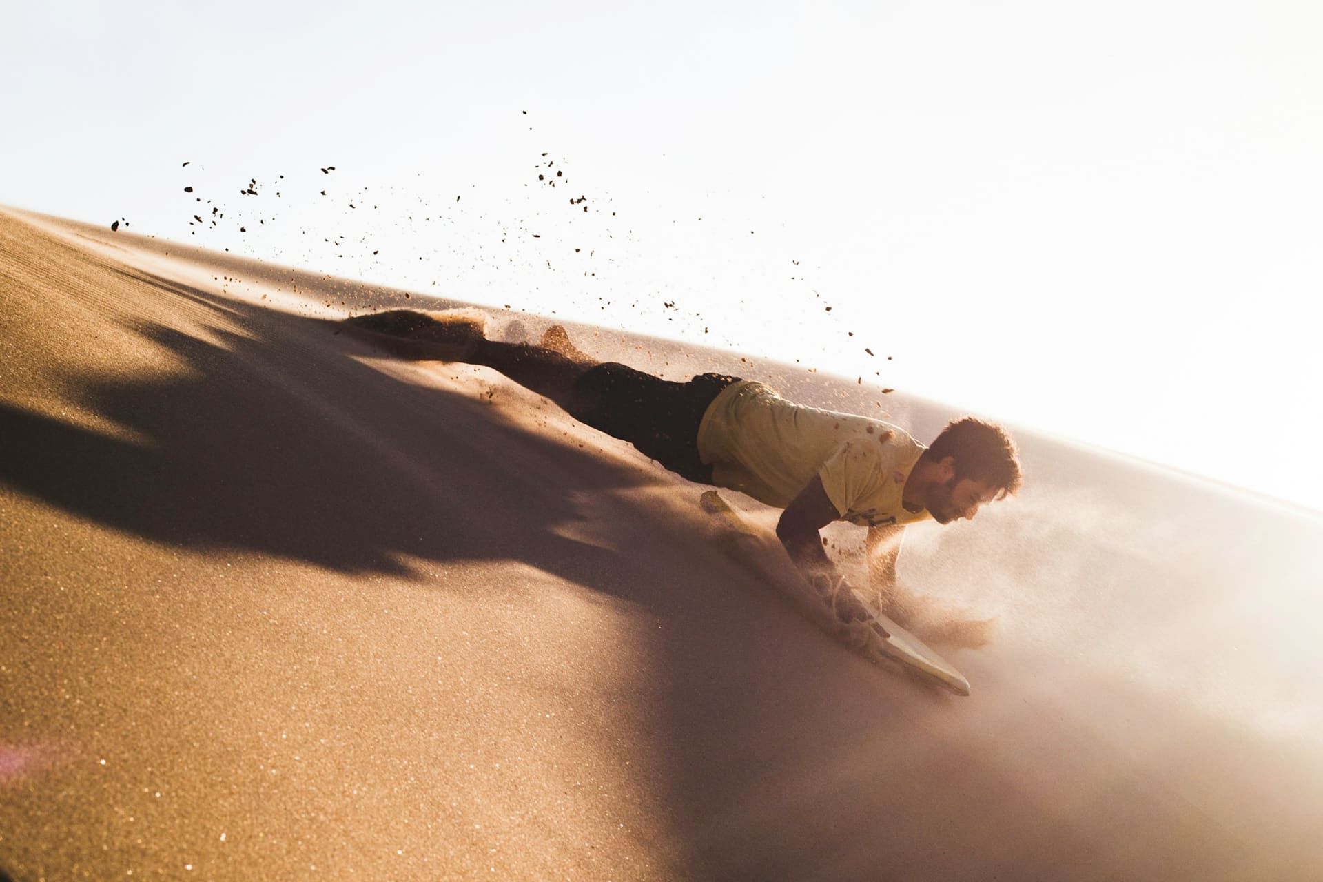 Sandboarder in mid-descent on a waxed board down a Lahbab dune face on a Dubai desert safari at golden hour