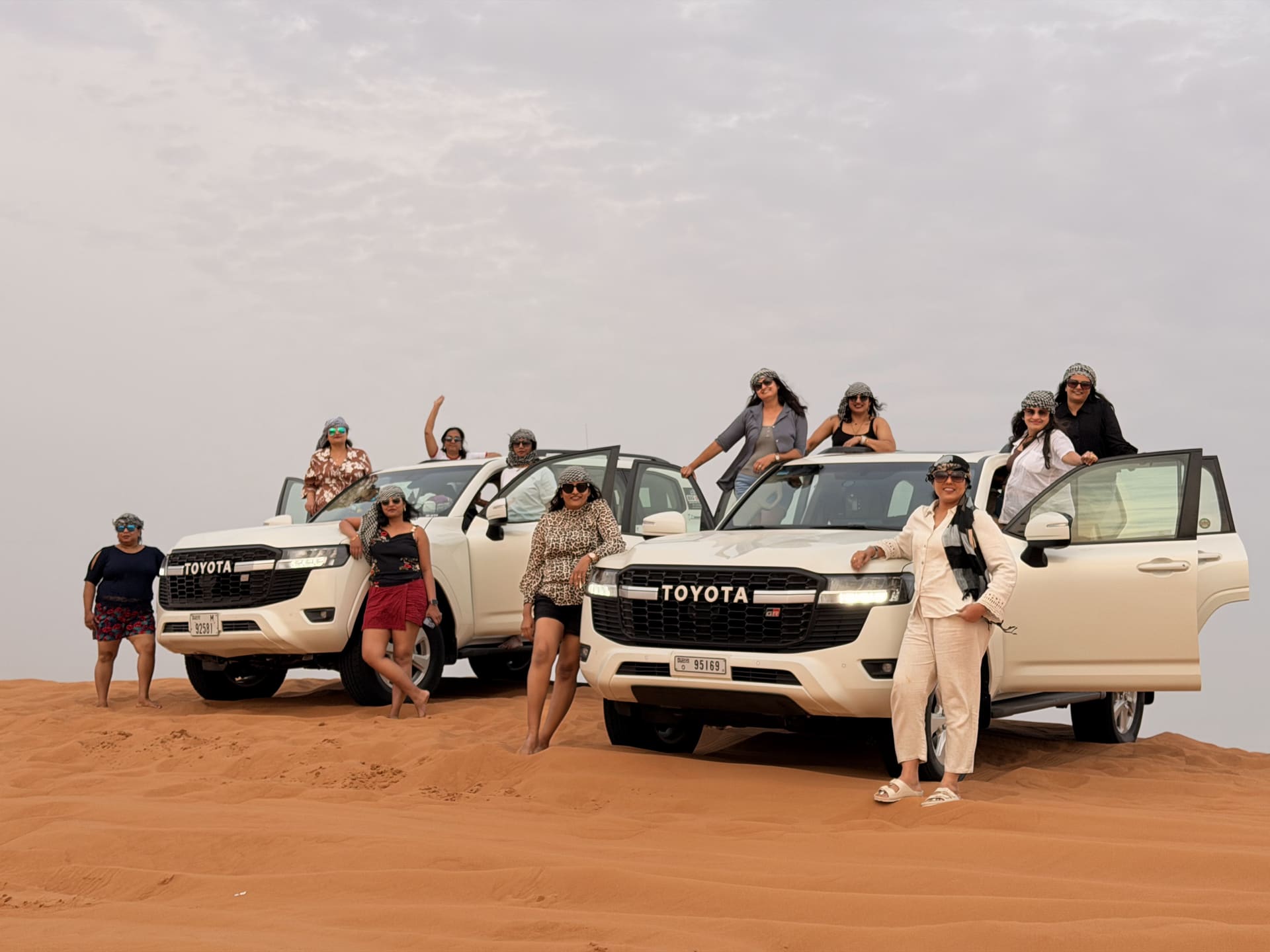 Group of guests around two white Toyota Land Cruisers on red dunes