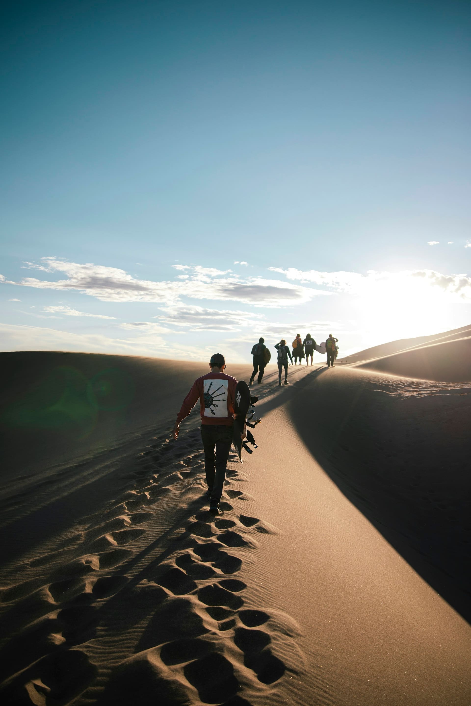 A line of footprints crossing a high crescent dune at golden hour
