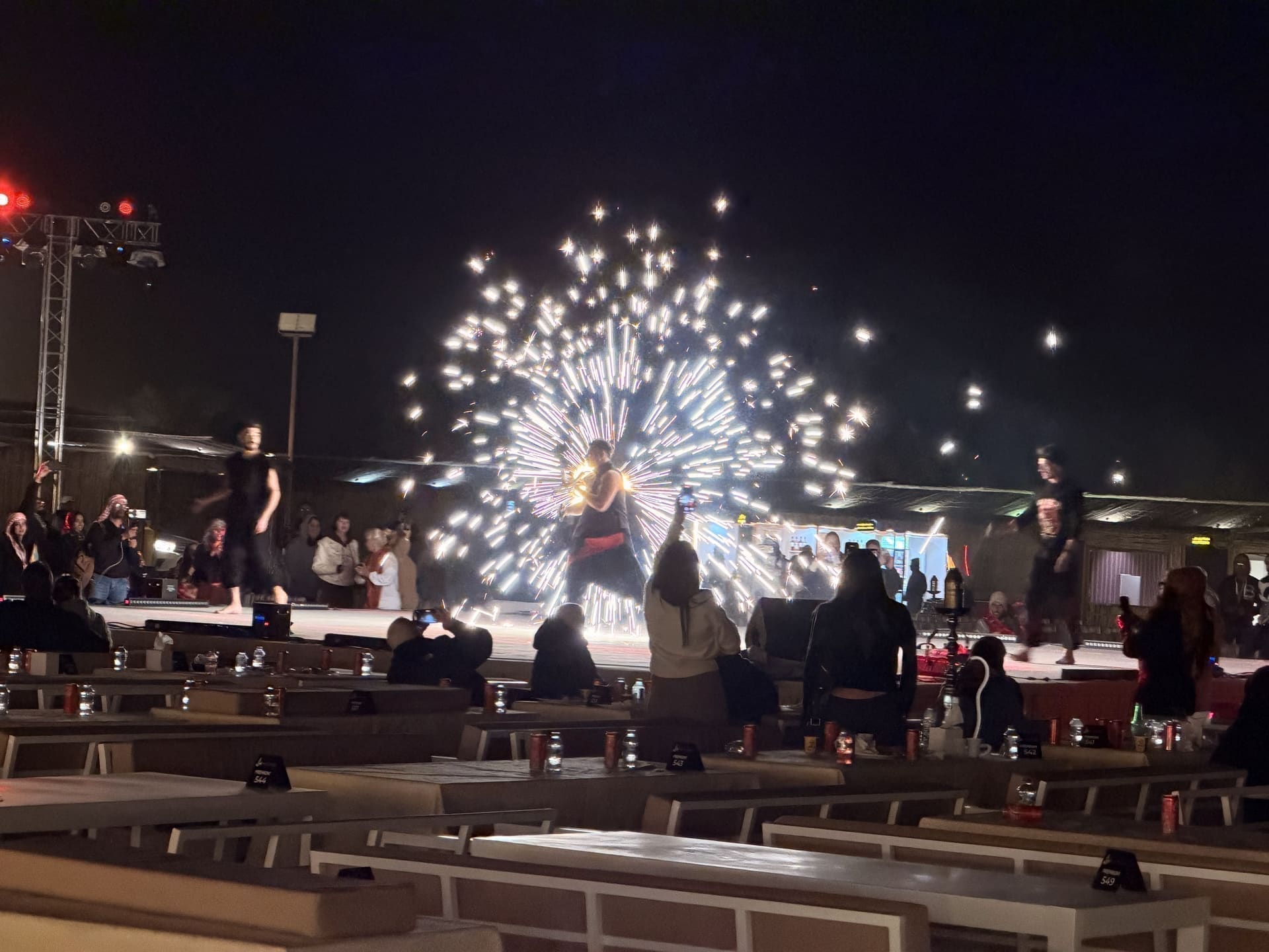 Fire spinner performing on stage at a night desert camp with seated guests