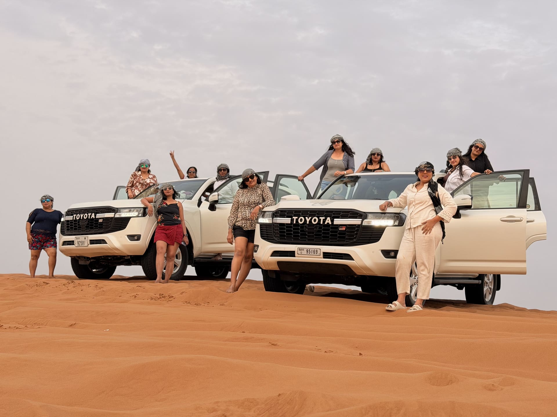 Guests celebrating around white Toyota Land Cruisers on the Dubai dunes