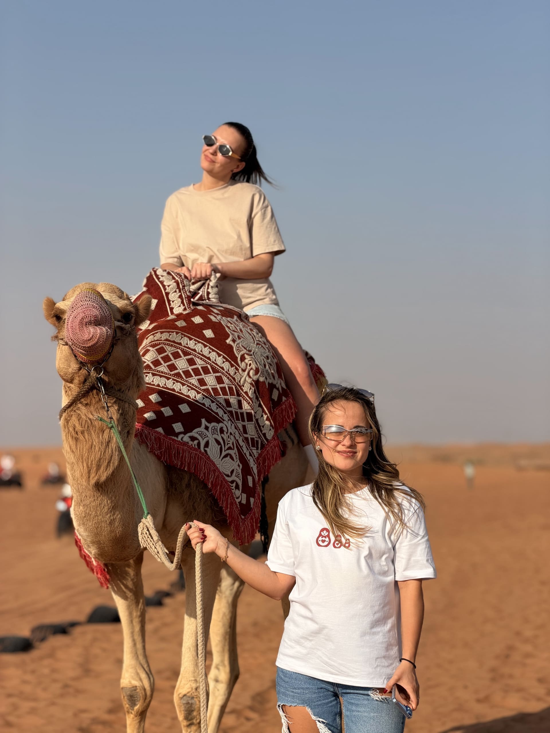 Guest riding a decorated camel with a handler walking alongside at golden hour