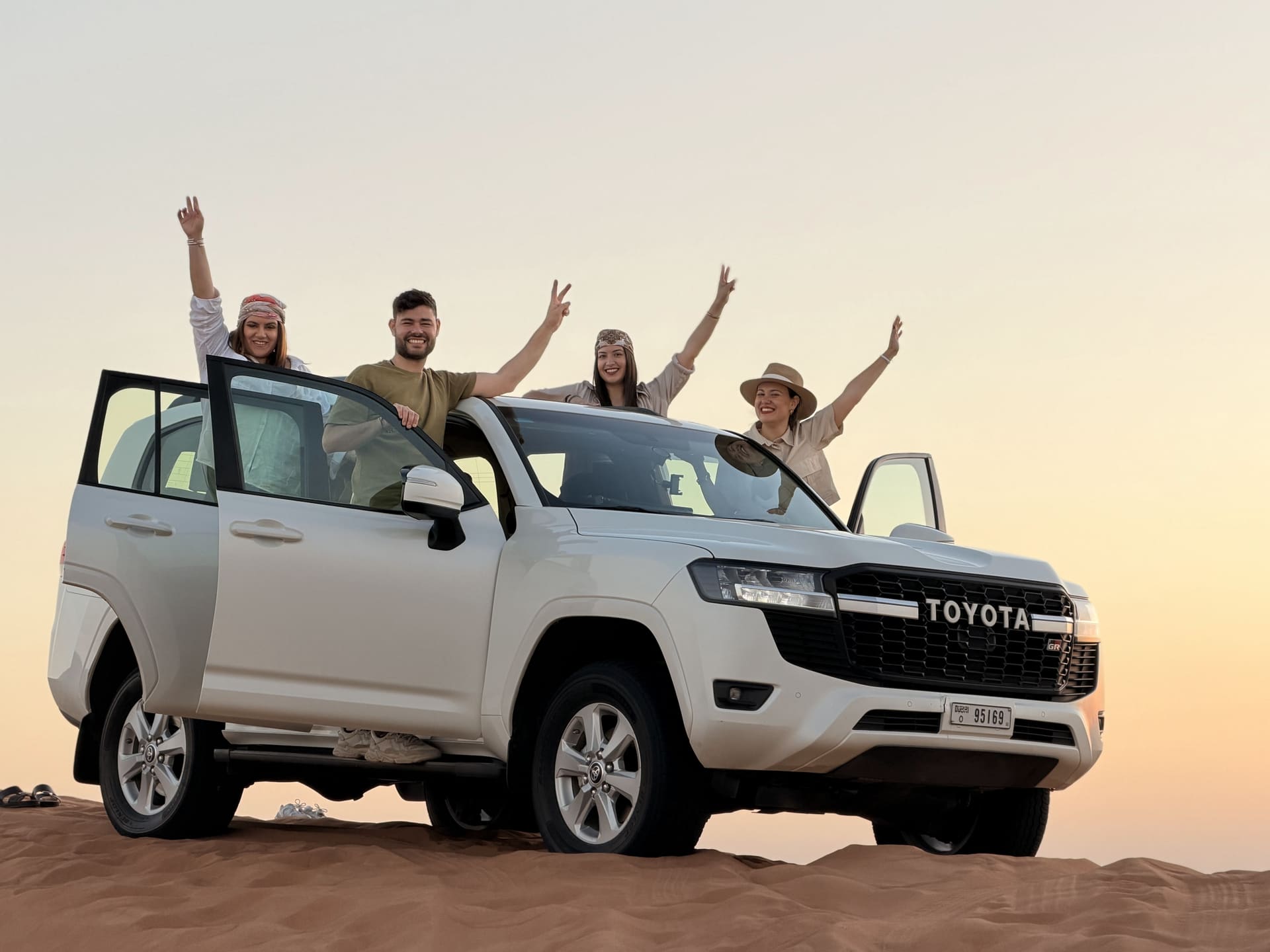Guests leaning from a white Toyota Land Cruiser at sunset
